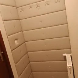 Ukończona realizacja: beżowe panele tapicerowane na ścianie w przedpokoju, z wieszakami i dekoracyjnymi guzikami, tworzące miękkie wykończenie wnętrza.