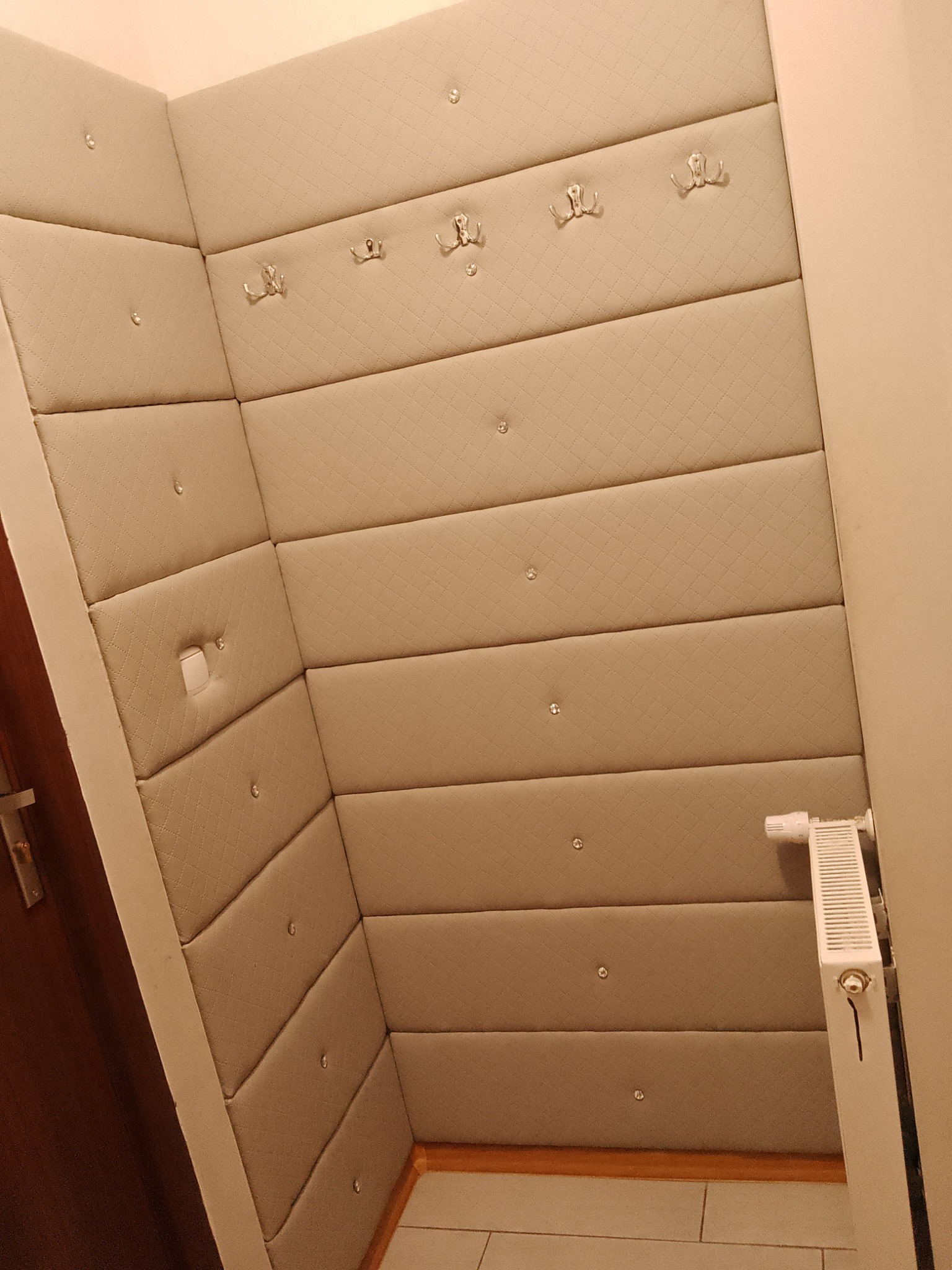 Ukończona realizacja: beżowe panele tapicerowane na ścianie w przedpokoju, z wieszakami i dekoracyjnymi guzikami, tworzące miękkie wykończenie wnętrza.