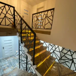 Schody z podświetlanymi stopniami i nowoczesną, geometryczną balustradą z metalu. Widok z góry, ciepłe oświetlenie wnętrza, marmurowe wykończenie.