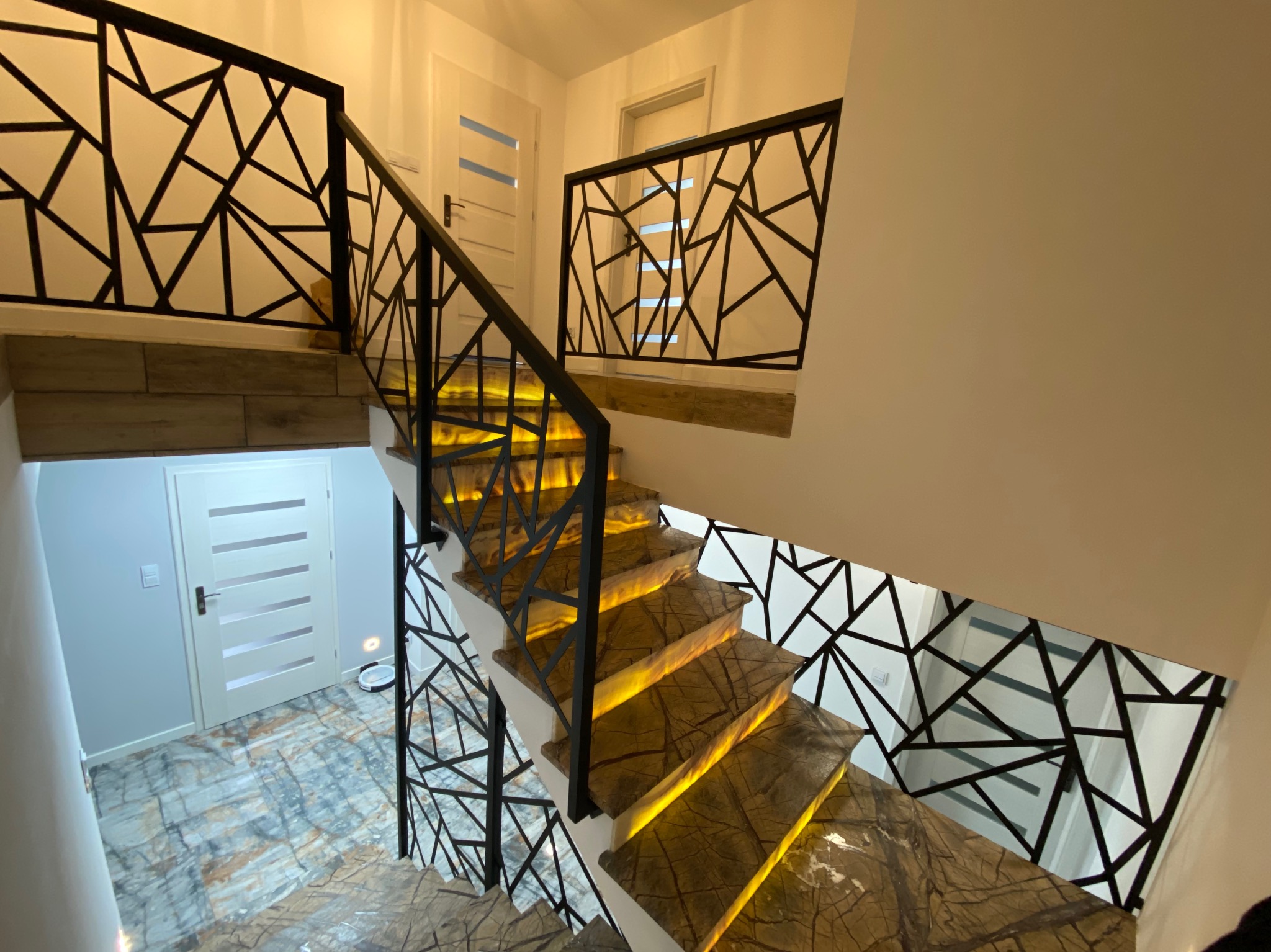 Schody z podświetlanymi stopniami i nowoczesną, geometryczną balustradą z metalu. Widok z góry, ciepłe oświetlenie wnętrza, marmurowe wykończenie.