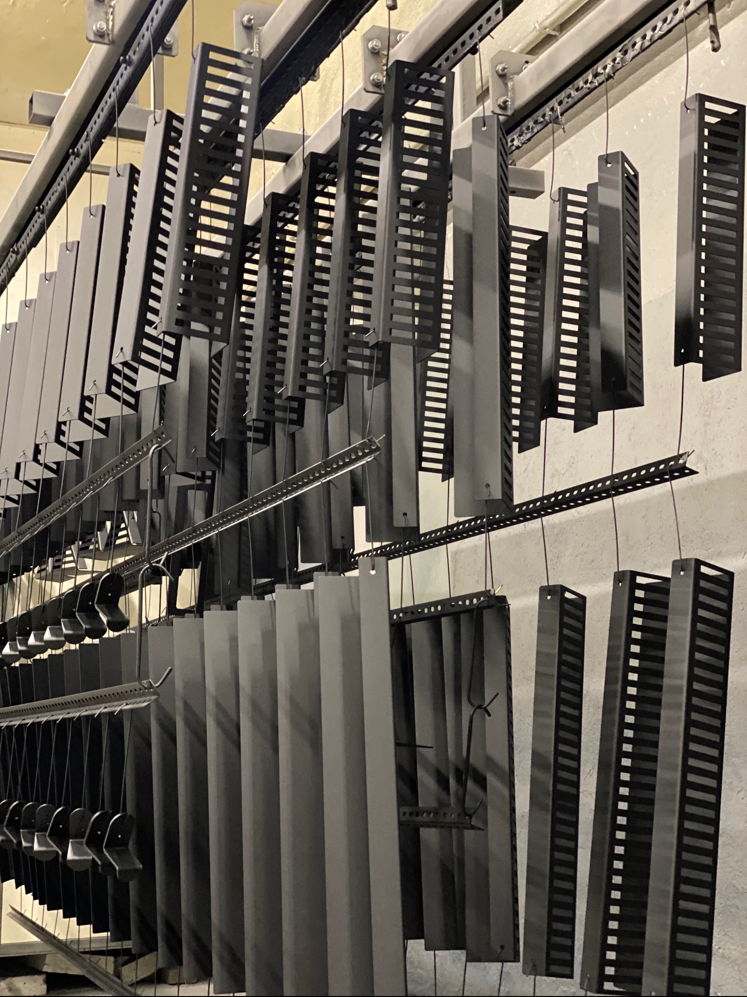 Elementy metalowe po procesie malowania proszkowego zawieszone na wieszakach w Wohyniu. Widoczne detale z perforacją i pełne panele.