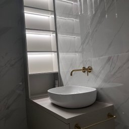 Tomson Company Ewa Ordziniak - Nowoczesna łazienka z marmurowymi płytkami, okrągłą umywalką nablatową, złotą armaturą i podświetlaną szafką wnękową. Minimalistyczny design, eleganckie wykończenie.