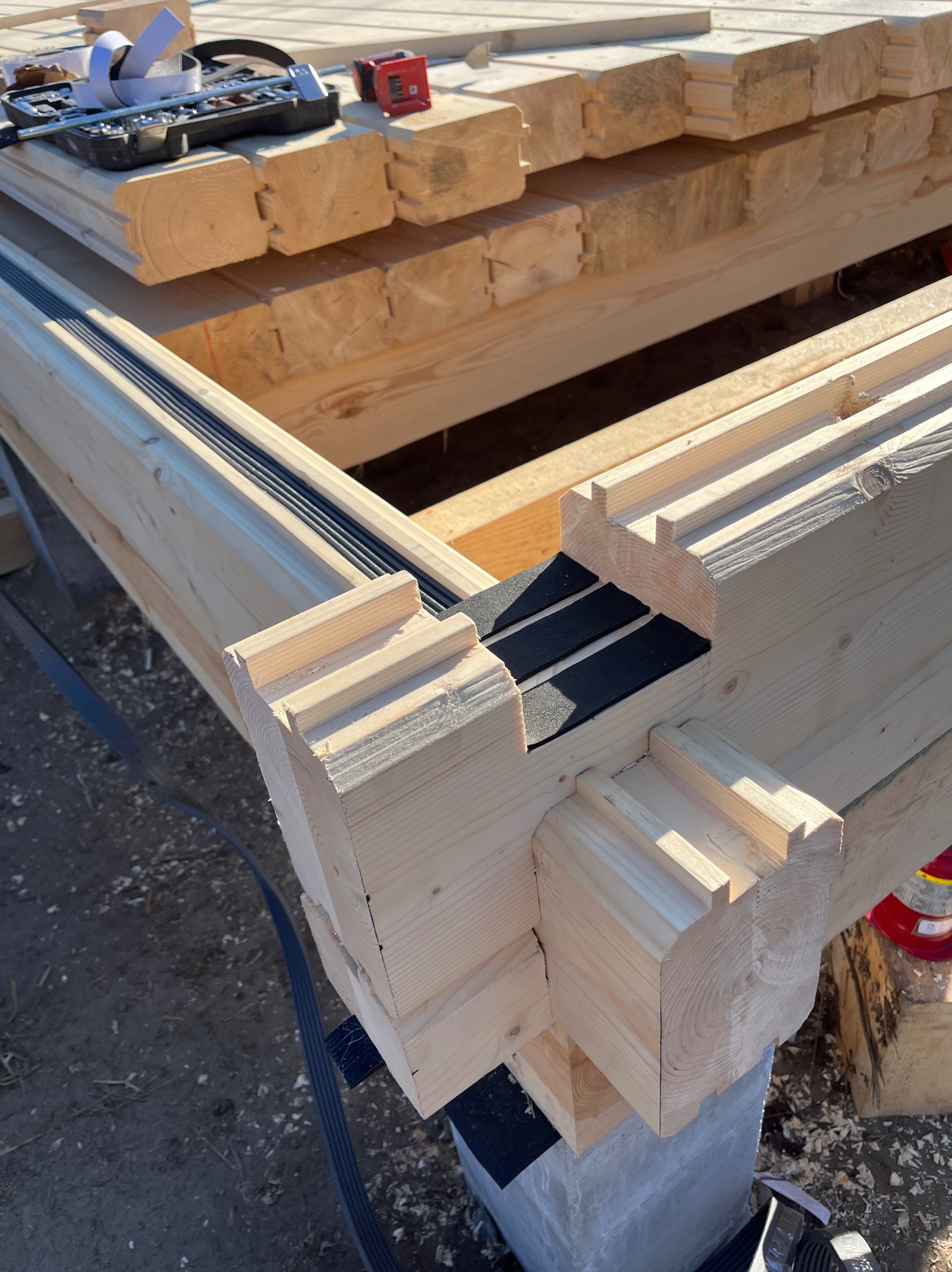 Fragment konstrukcji domu szkieletowego z drewnianych bali, widoczne połączenia i izolacja. Na górze narzędzia i materiały budowlane.