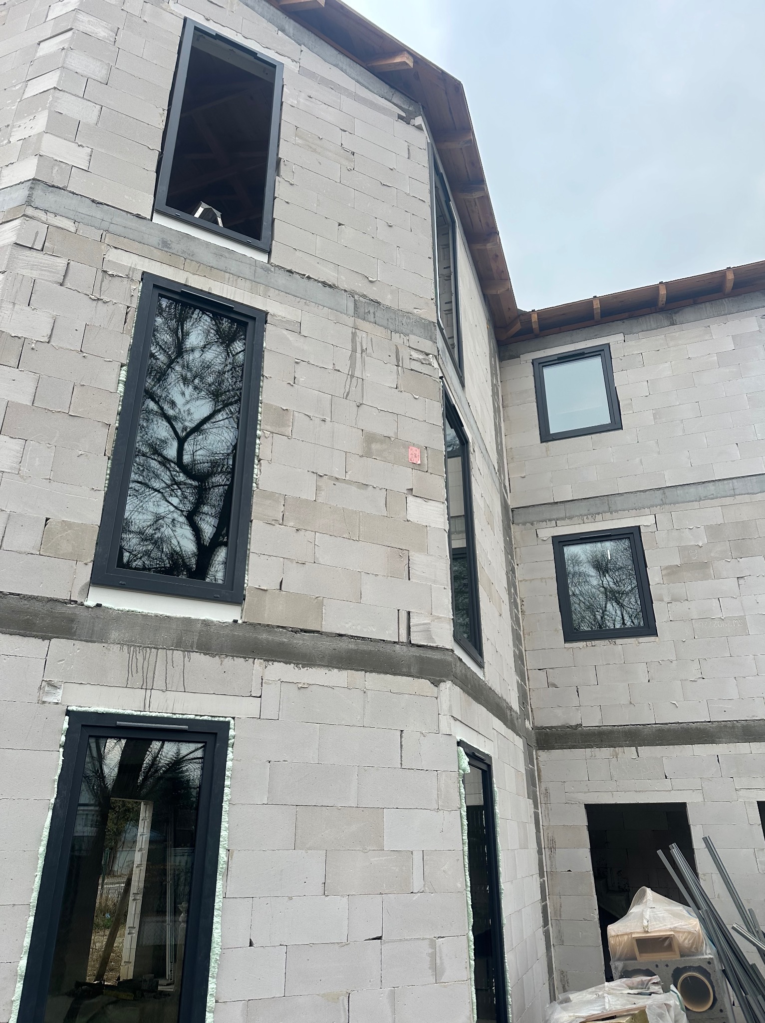 Surowy budynek z betonu komórkowego w trakcie montażu czarnych okien. Widoczne pianowanie wokół ram okiennych. Ujęcie z dołu, pochmurne niebo w tle.