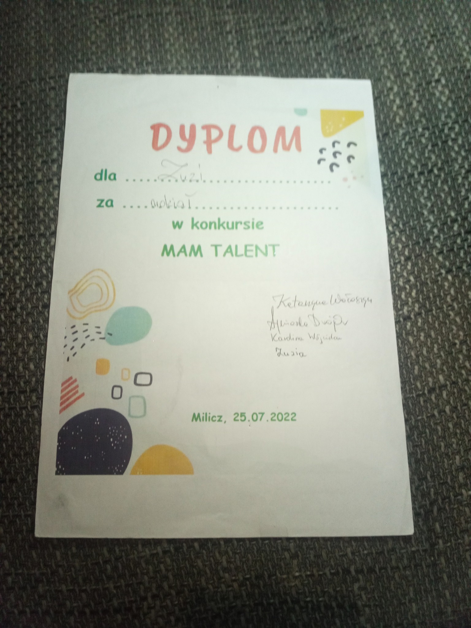 Dyplom dla Zuzi za udział w konkursie MAM TALENT, z podpisami, datowany na 25.07.2022, leży na szarej powierzchni.