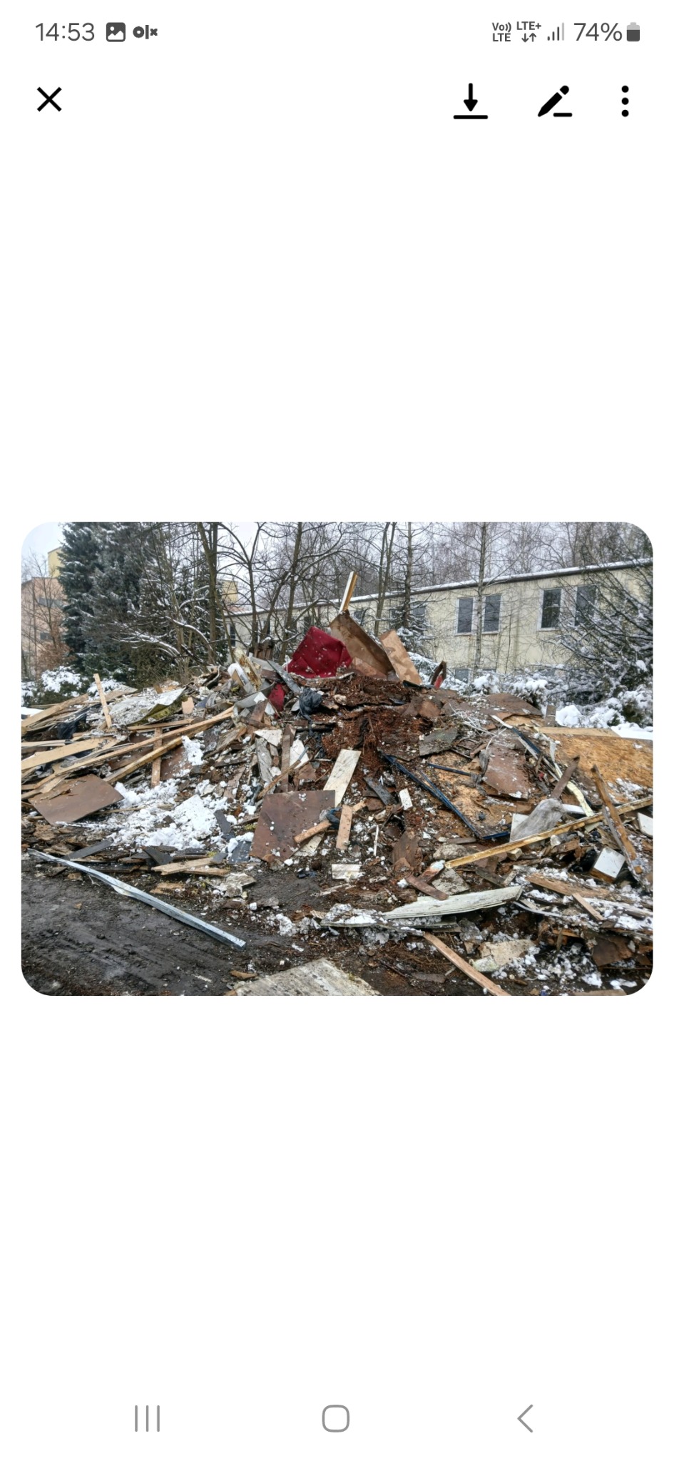 Sterta gruzu i odpadów po rozbiórce na śniegu, z fragmentem czerwonego mebla. W tle budynek i drzewa.