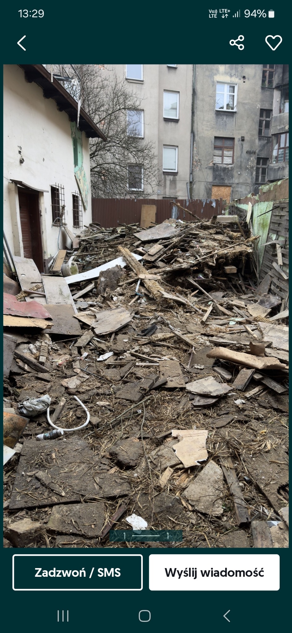 Sterta gruzu i odpadów po rozbiórce, z elementami drewnianymi i betonowymi, na tle budynku mieszkalnego i fragmentu zabudowań gospodarczych.