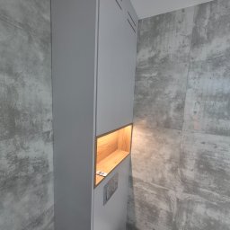 Ytsenko Dmytro - Szara szafka łazienkowa na wymiar z drewnianą wnęką oświetloną ciepłym światłem, dopasowana do płytek imitujących beton. Minimalistyczny design, nowoczesne wykończenie.