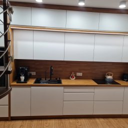 Ytsenko Dmytro - Nowoczesna kuchnia z białymi frontami i drewnianym blatem, oświetleniem LED pod szafkami wiszącymi, spiralne schody z boku. Minimalistyczny design.