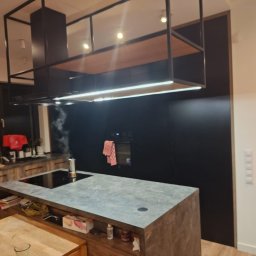 Ytsenko Dmytro - Nowoczesna kuchnia z wyspą i czarnym panelem ściennym. Nad wyspą konstrukcja z oświetleniem LED. Na blacie ekspres do kawy.