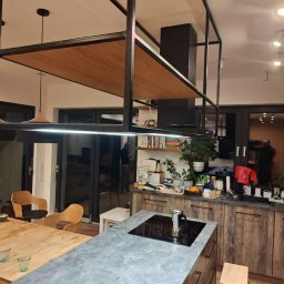 Ytsenko Dmytro - Nowoczesna kuchnia z wyspą i blatem imitującym beton. Nad wyspą konstrukcja z metalu i drewna. Widoczne drewniane szafki i półki z dekoracjami. Minimalistyczny design.