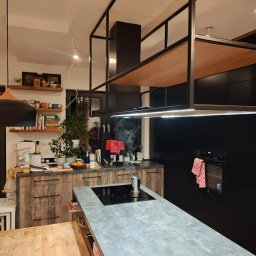 Ytsenko Dmytro - Nowoczesna kuchnia z wyspą i betonowym blatem. Na indukcji stoi zaparzacz do kawy, a nad wyspą designerski okap z drewnianą półką. Szafki w kolorze czerni i drewna.