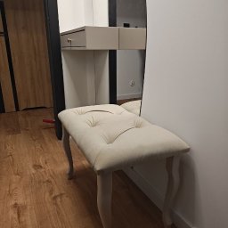 Ytsenko Dmytro - Toaletka z owalnym lustrem i tapicerowanym pufem w odcieniach beżu, na drewnianej podłodze. Widoczne detale: złoty uchwyt szuflady, dekoracyjne nóżki pufu.