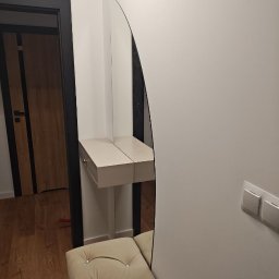 Ytsenko Dmytro - Nowoczesna toaletka z lustrem o nietypowym kształcie w przedpokoju. Beżowa pufa z guzikami i drewniana podłoga. Minimalistyczny design.