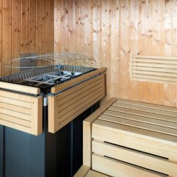 Ytsenko Dmytro - Jasne drewno w saunie: ławki z listew, piec z osłoną. Drewniane panele ścienne. Minimalistyczny design, ciepłe oświetlenie. Elementy wykończenia i wyposażenia sauny.