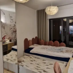 Pokój dziecięcy z łóżkiem wysuwanym i lustrzaną szafą. W tle widoczna lampa w stylu skandynawskim i zasłony. Na szafce nocnej lampka w kształcie królika.