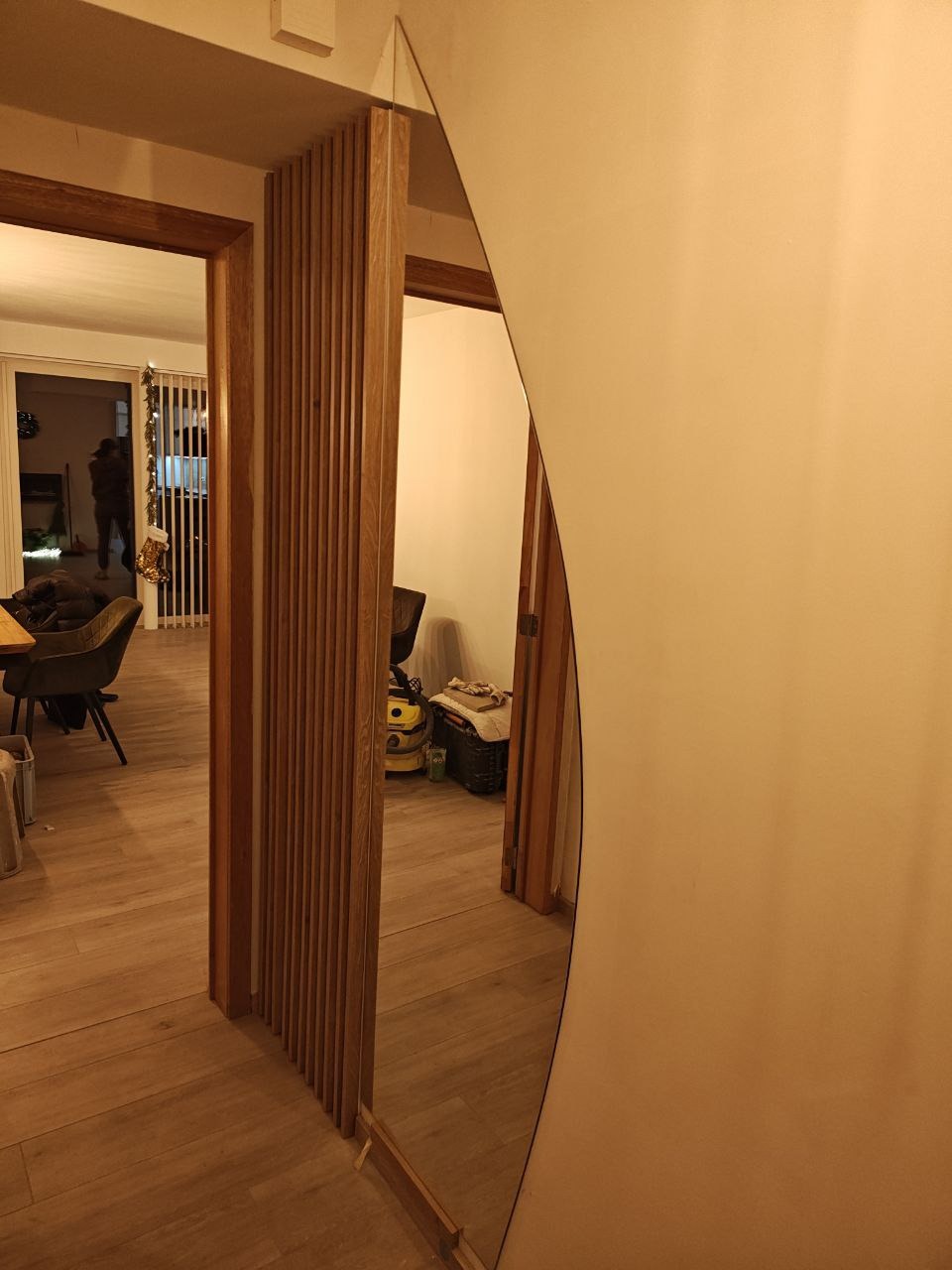 Nowoczesne drzwi przesuwne z drewnianymi lamelami, oddzielające przestrzeń w jasnym wnętrzu. Widoczne odbicie w lustrzanej powierzchni.