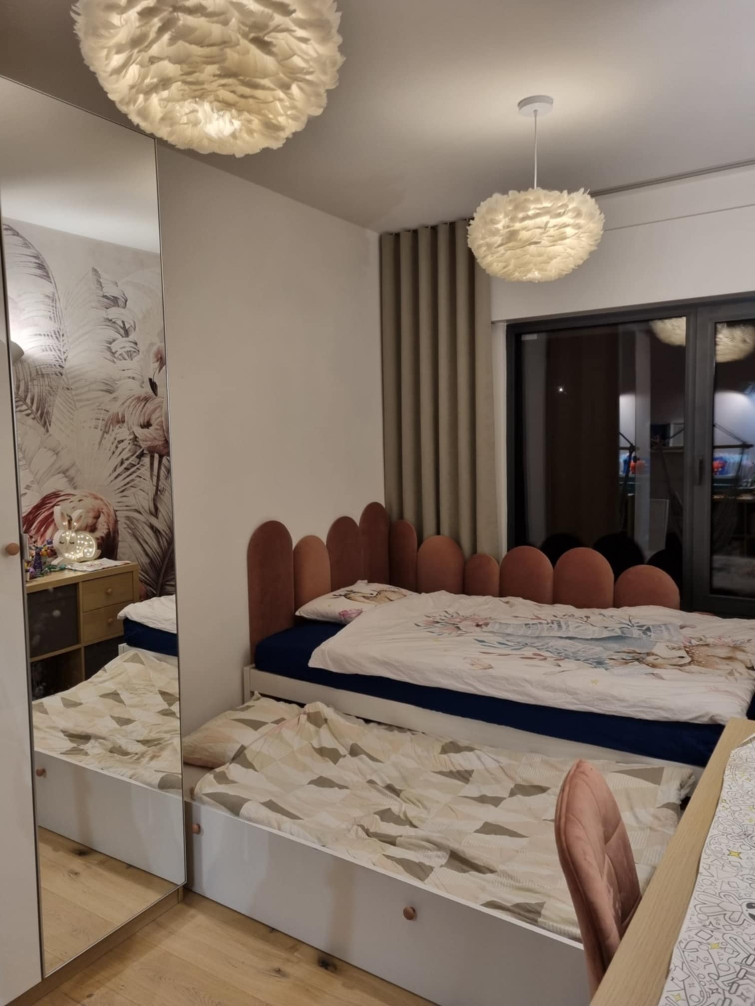 Pokój dziecięcy z łóżkiem wysuwanym i lustrzaną szafą. W tle widoczna lampa w stylu skandynawskim i zasłony. Na szafce nocnej lampka w kształcie królika.