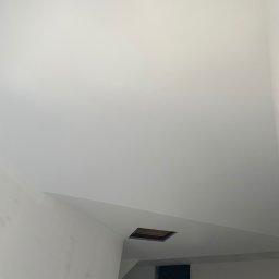 ZPRemBud Denys Shvets - Białe, świeżo pomalowane wnętrze z otworem w suficie i ścianie. Widoczny fragment sufitu i ściany, proste linie, minimalistyczny kadr. Otwór wentylacyjny w suficie i otwór w ścianie.
