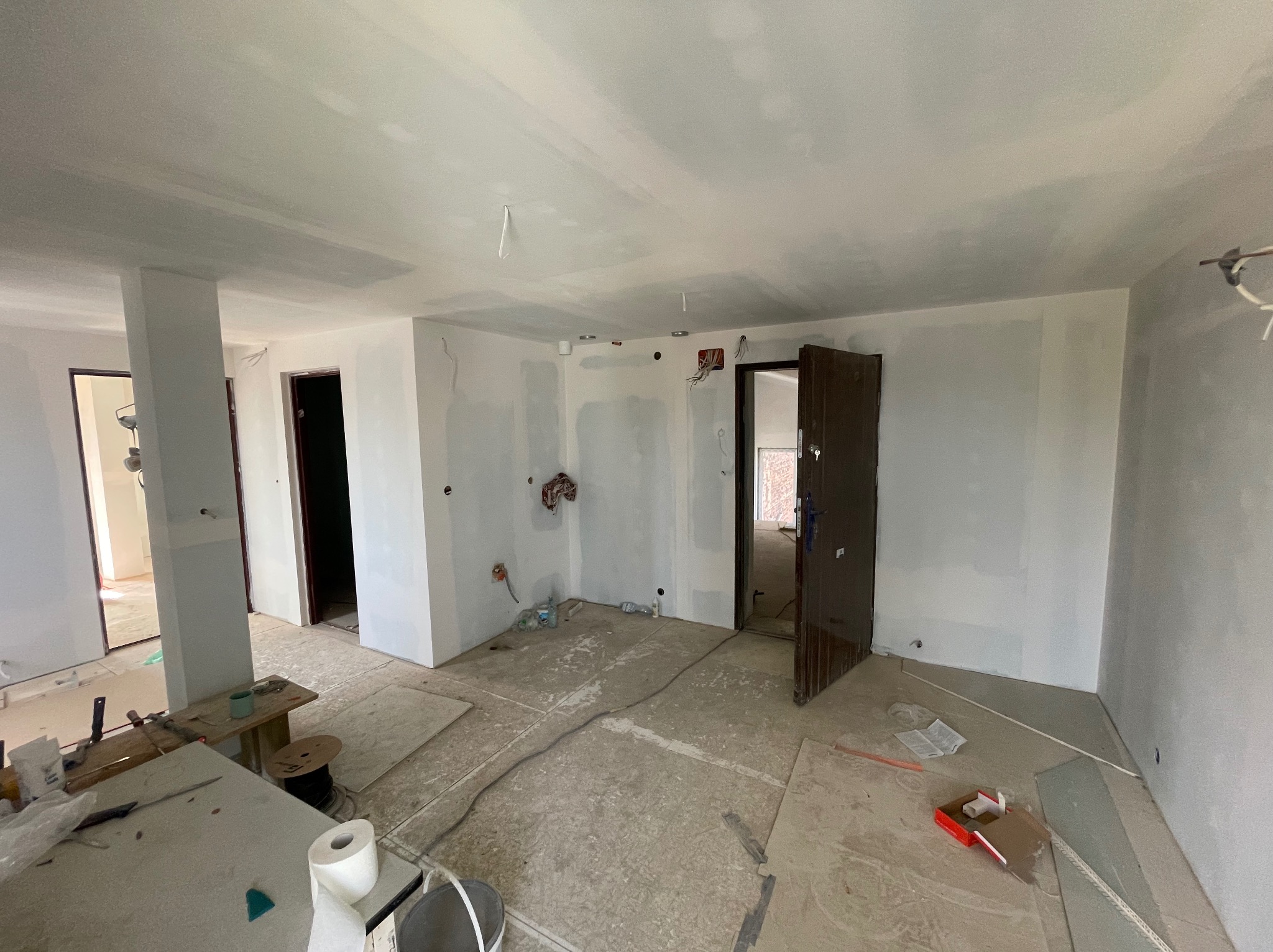 Wnętrze w trakcie prac: ściany po szpachlowaniu, widoczne kable i instalacje elektryczne, otwarte drzwi, przygotowanie do dalszych prac wykończeniowych.