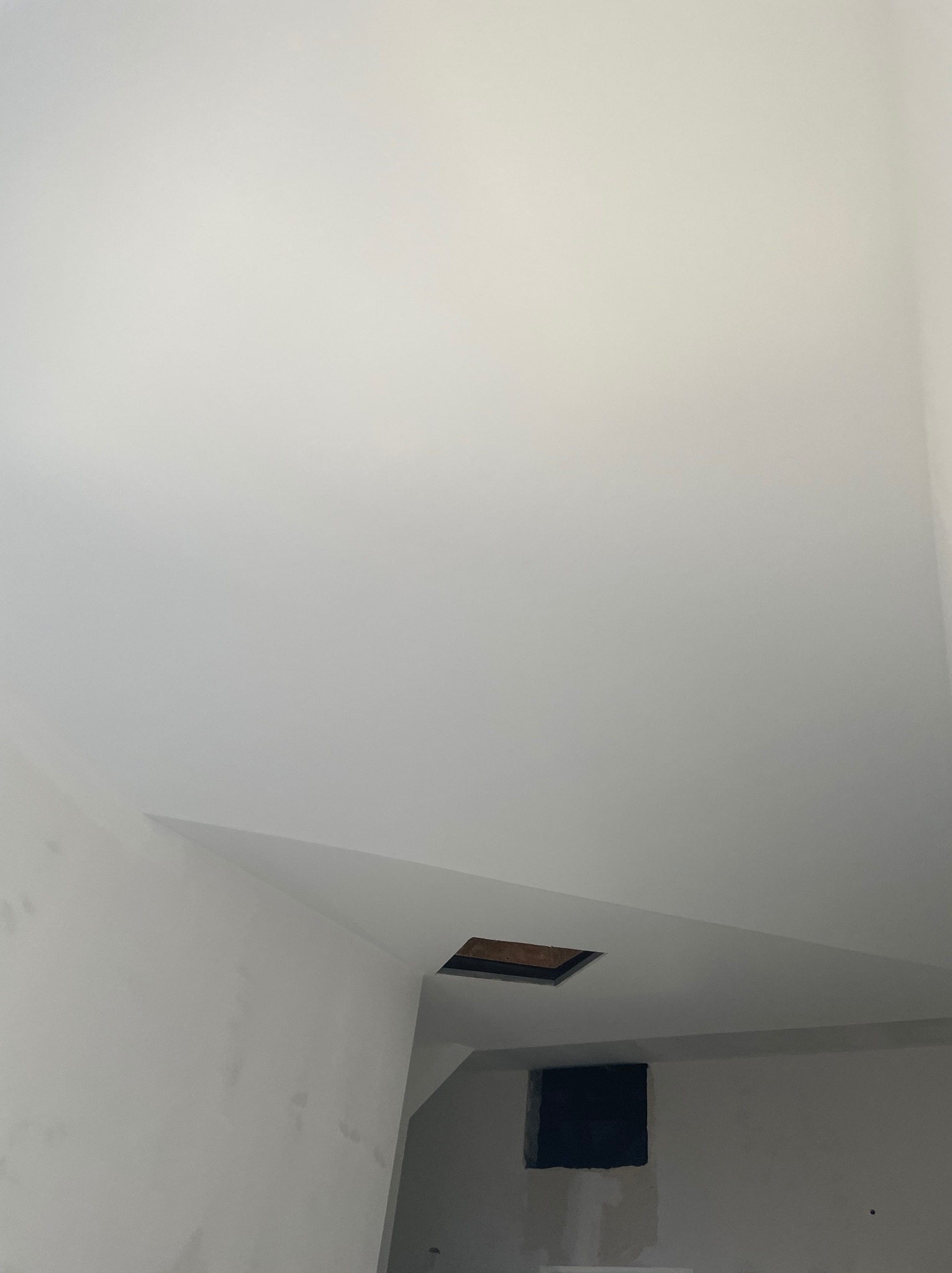 Białe, świeżo pomalowane wnętrze z otworem w suficie i ścianie. Widoczny fragment sufitu i ściany, proste linie, minimalistyczny kadr. Otwór wentylacyjny w suficie i otwór w ścianie.
