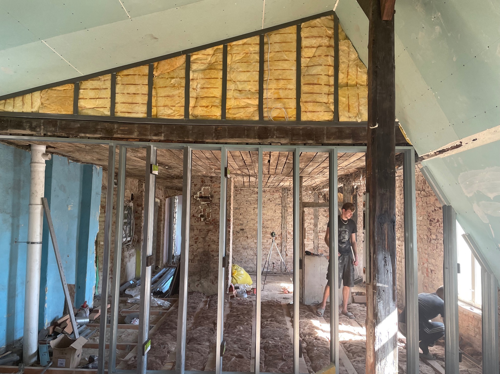 Poddasze w trakcie adaptacji: widoczne ocieplenie wełną mineralną, metalowy szkielet ścian działowych i fragment płyty gipsowo-kartonowej na skośnym suficie.