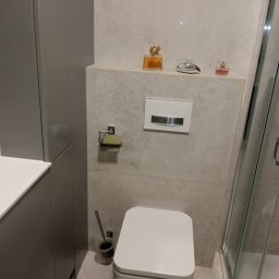 ProPerfect - Nowoczesna toaleta w jasnej łazience z szarymi szafkami, widok z góry. Na półce dekoracyjne flakoniki perfum. Minimalistyczny design i neutralna kolorystyka.