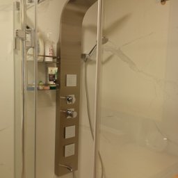 ProPerfect - Nowoczesna kabina prysznicowa z panelem natryskowym ze stali nierdzewnej, półką na kosmetyki i marmurowymi ścianami. Widoczne detale wykończenia.