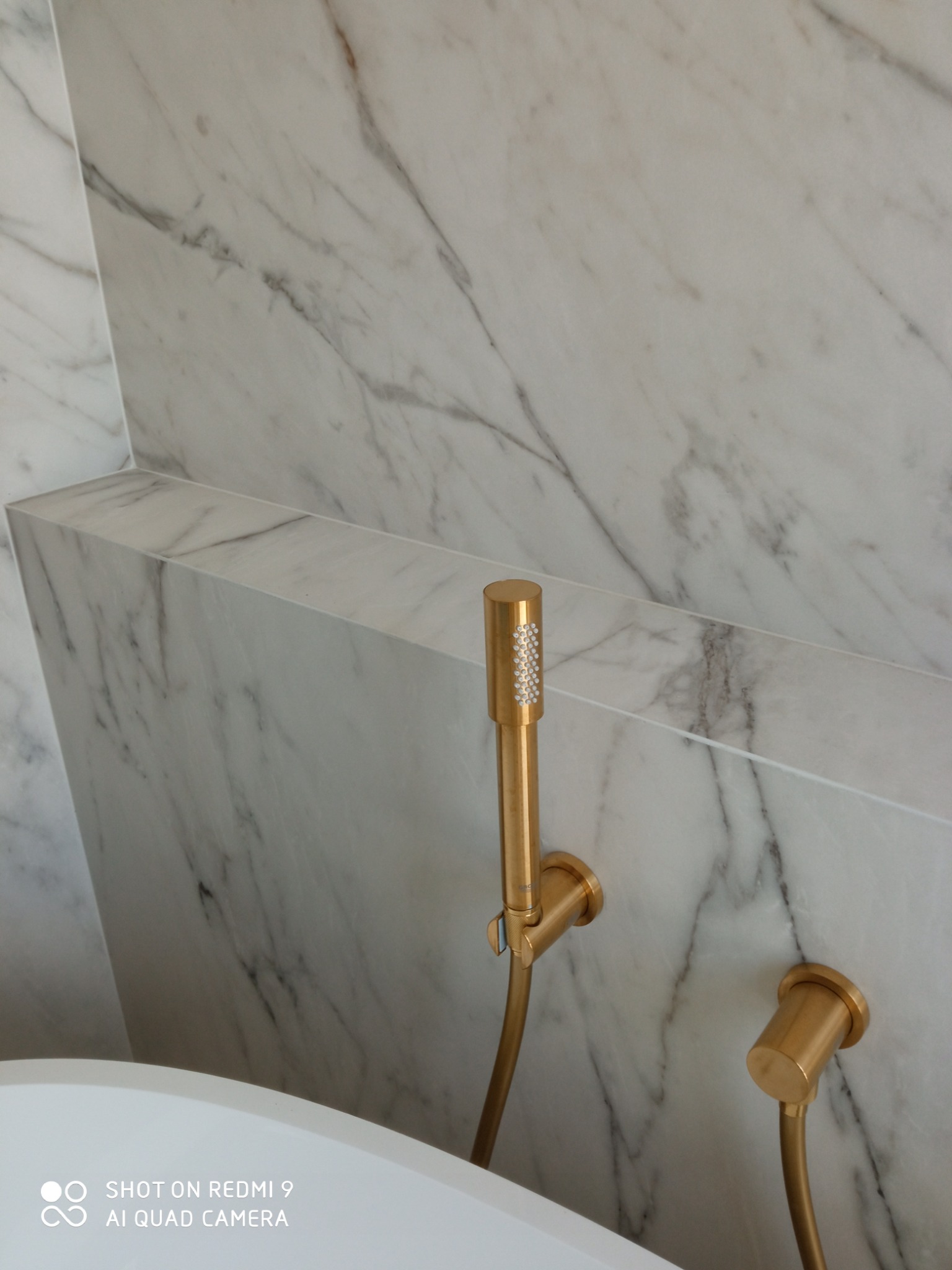 Bateria prysznicowa w kolorze złotym na tle marmurowej ściany w wykończonej łazience. Minimalistyczny design i eleganckie detale.