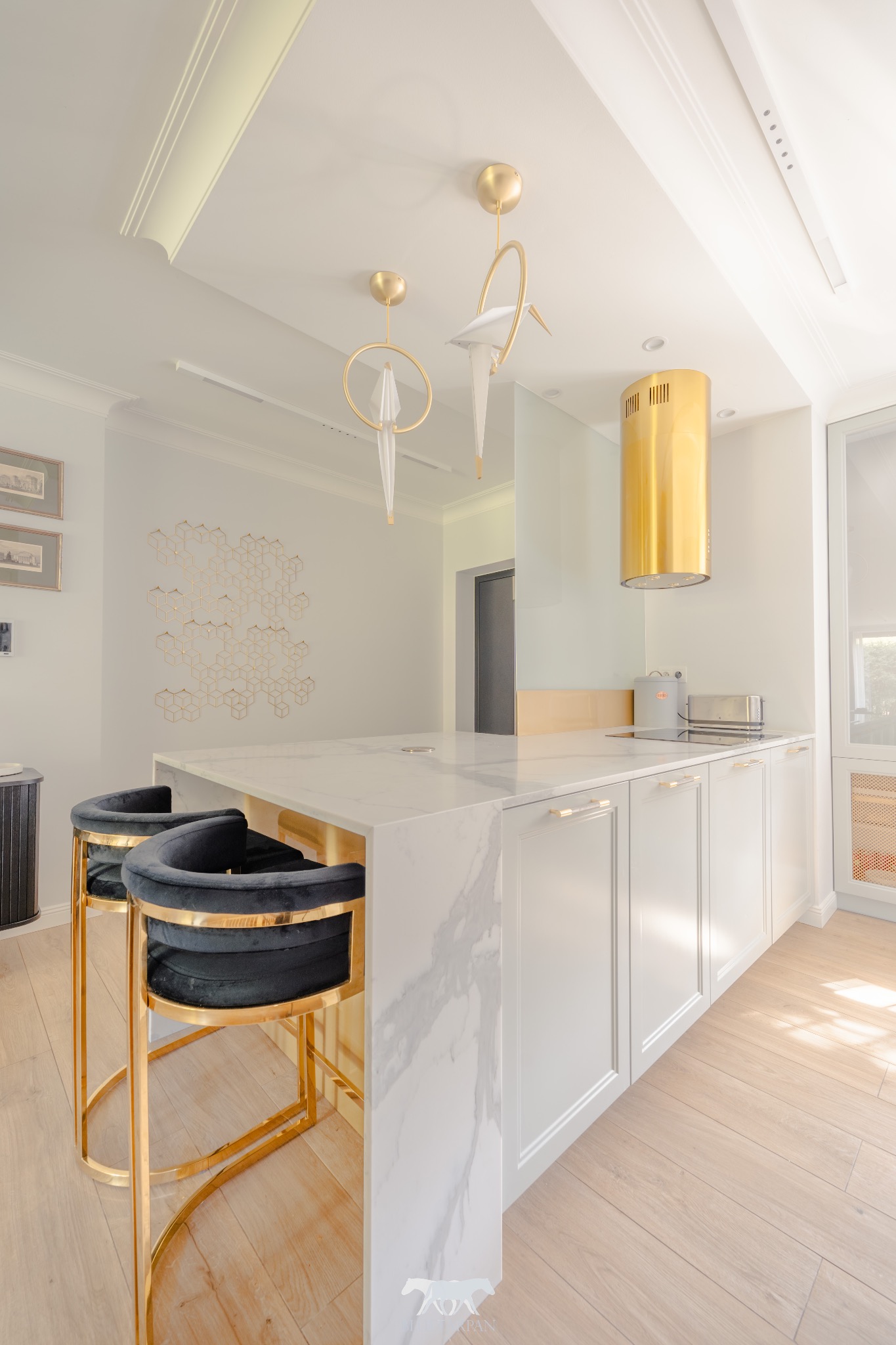 Elegancka kuchnia z marmurowym blatem, złotymi akcentami i designerskimi krzesłami barowymi. Nowoczesne oświetlenie i minimalistyczny okap w kolorze złota.