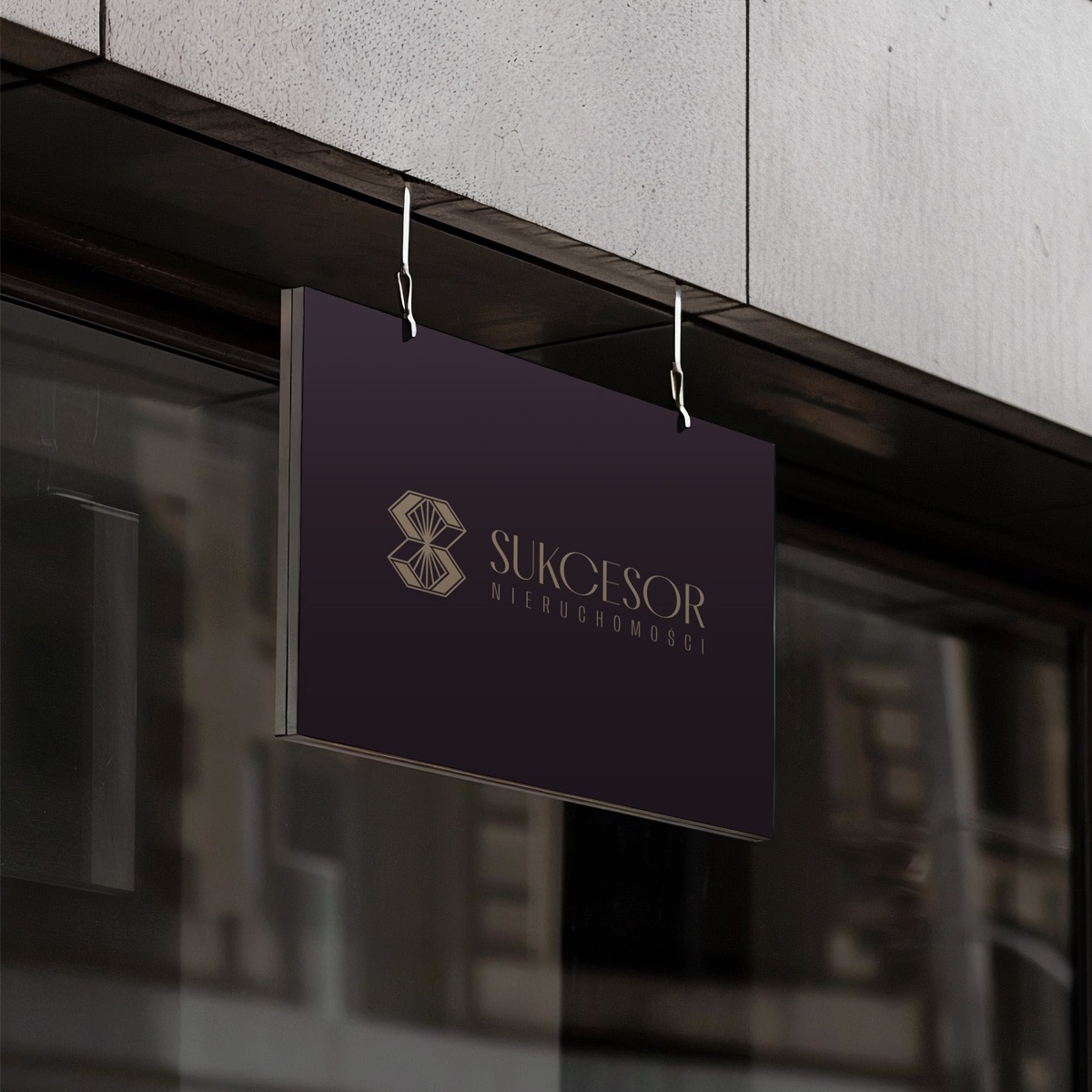 Elegancki szyld firmy Sukcesor Nieruchomości, zawieszony na metalowych haczykach, z logo w kolorze złota na ciemnym tle, widoczny z perspektywy ulicy.