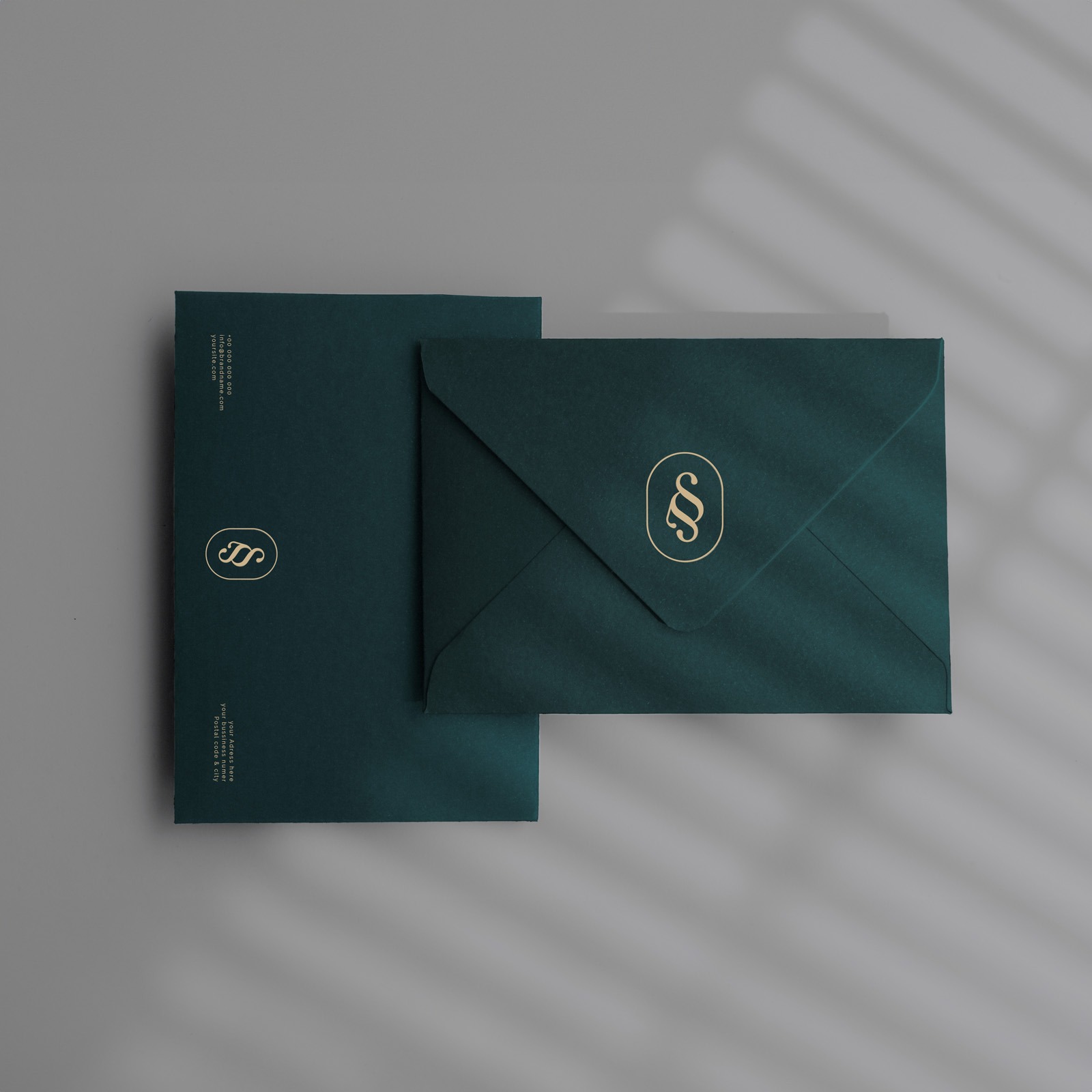 Elegancki, szmaragdowy zestaw papeterii z logo prawniczym w złotym kolorze, na tle z cieniem rzucanym przez żaluzje. Minimalistyczny design, luksusowa estetyka.