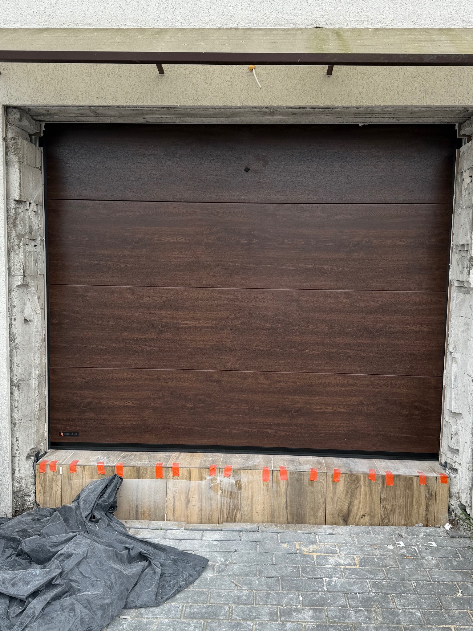 Montaż brązowej bramy garażowej segmentowej w Słupsku. Widoczne detale mocowania i zabezpieczenia. Brama z poziomymi panelami o strukturze drewna.