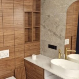 REFORMA REMONT W FORMIE SPÓŁKA Z OGRANICZONĄ ODPOWIEDZIALNOŚCIĄ - Nowoczesna łazienka z drewnianą zabudową, marmurową ścianą i owalną umywalką. Lustro w kształcie łuku odbija niebieską ścianę. Minimalistyczny design.