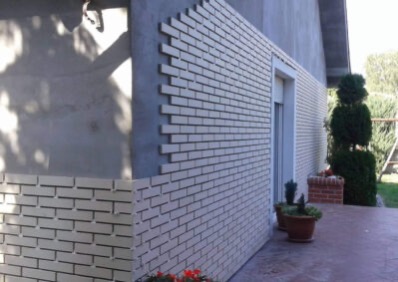 Elewacja domu z klinkieru w trakcie montażu. Widoczne fragmenty ściany bez okładziny i świeżo położony klinkier w jasnym odcieniu. Ujęcie z zewnątrz.