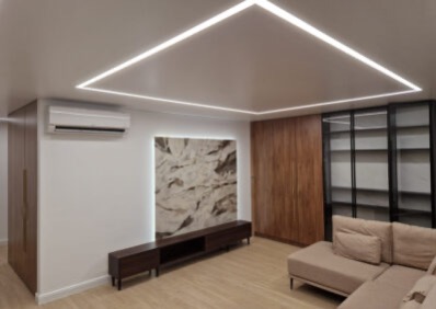 Nowoczesny salon z podświetlanym sufitem w kształcie kwadratu, drewnianą zabudową i beżową sofą narożną. Minimalistyczny design z obrazem na ścianie.