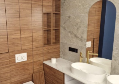 Nowoczesna łazienka z drewnianą zabudową, marmurową ścianą i owalną umywalką. Lustro w kształcie łuku odbija niebieską ścianę. Minimalistyczny design.