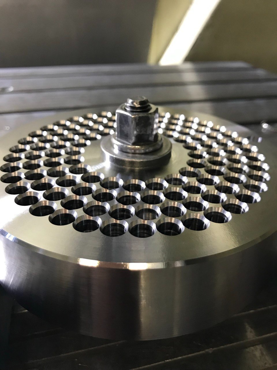 Metalowy element z precyzyjnie wywierconymi otworami, mocowany śrubą. Widoczna obróbka powierzchni. Detal z bliska, wykonany z dbałością o szczegóły.