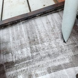 Gracjan Skalski - Uszczelnianie dachu papą termozgrzewalną na płaskiej powierzchni z użyciem palnika, z widoczną czerwoną linią wyznaczającą obszar roboczy.