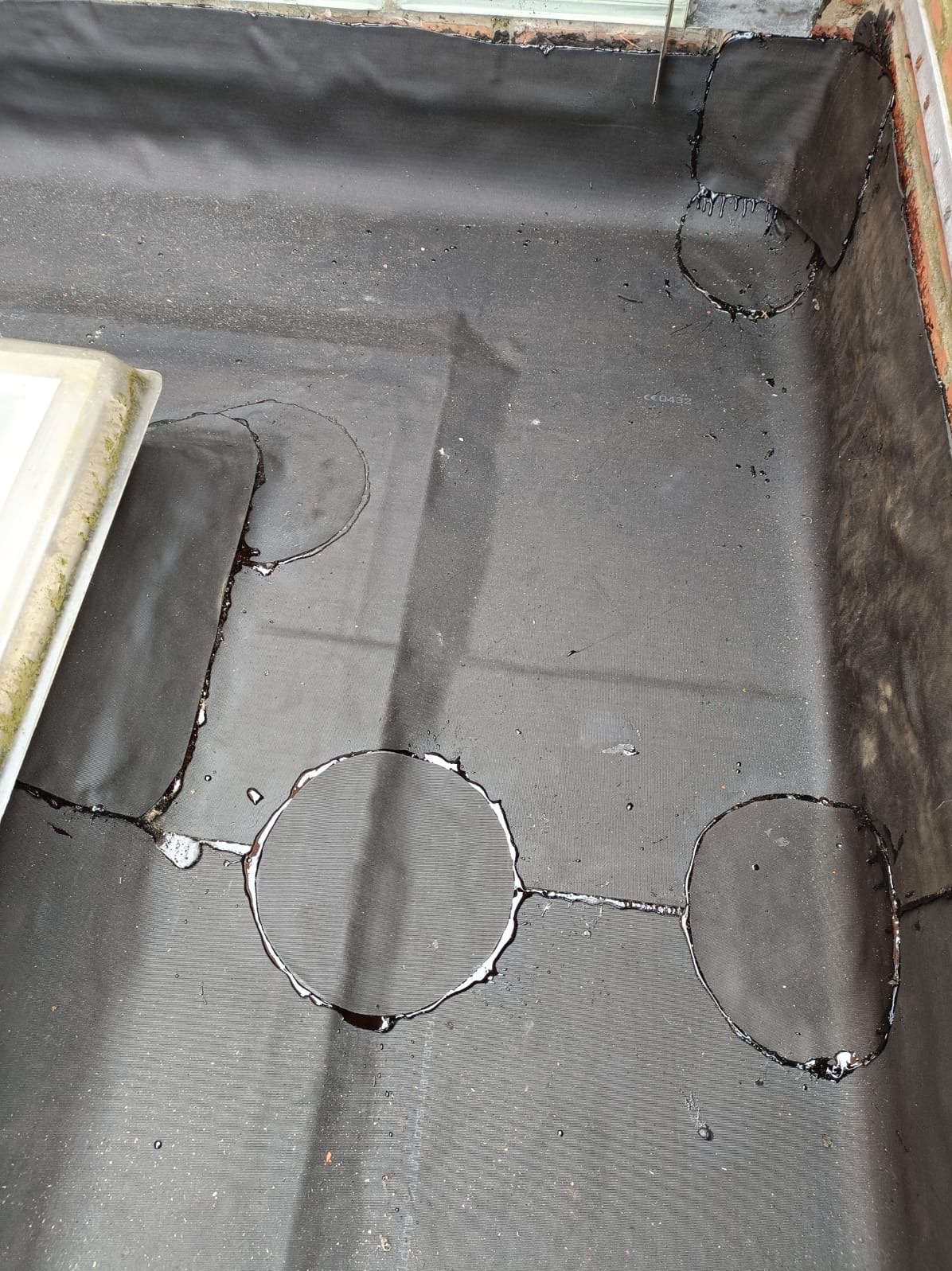 Czarna papa z widocznymi okrągłymi uszkodzeniami/przeciekami, prawdopodobnie do naprawy. Widoczne ślady wody i uszkodzeń.