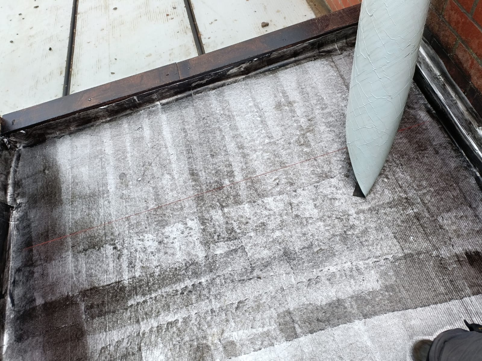 Uszczelnianie dachu papą termozgrzewalną na płaskiej powierzchni z użyciem palnika, z widoczną czerwoną linią wyznaczającą obszar roboczy.