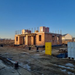 AJON SPÓŁKA Z OGRANICZONĄ ODPOWIEDZIALNOŚCIĄ - Budowa domu jednorodzinnego w stanie surowym otwartym, z widocznymi elementami zbrojenia i pustakami Porotherm. Na pierwszym planie żółta skrzynka gazowa.