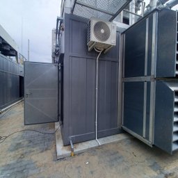 Klima4you Rafał Rabczak - Zewnętrzna instalacja klimatyzacyjna z jednostką na szarej obudowie, widoczne rury i elementy konstrukcyjne. Otwarta metalowa obudowa z kratką wentylacyjną.