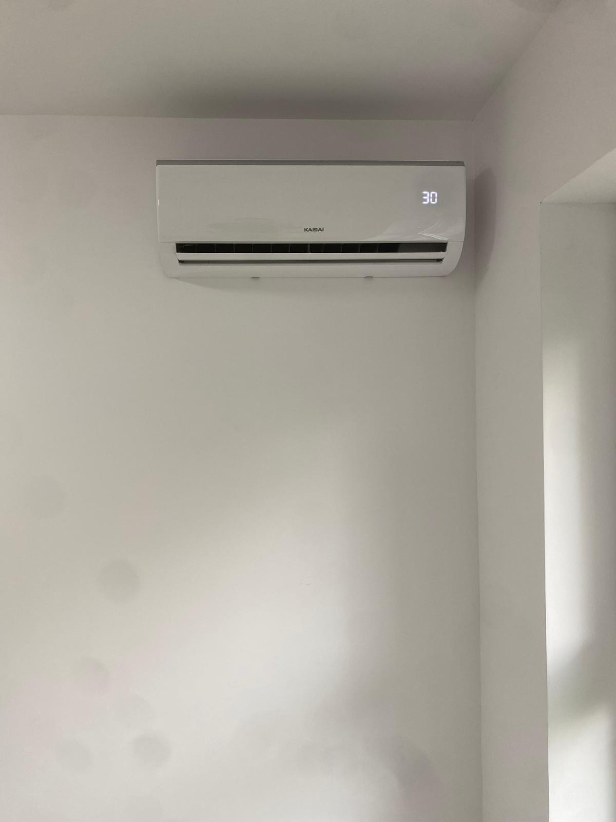 Biała klimatyzacja Kaisai z wyświetlaczem 30 stopni Celsjusza, zamontowana na gładkiej, białej ścianie w rogu pokoju. Minimalistyczny design.