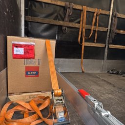 Kewin Grzybowski - Karton zabezpieczony pasami w przestrzeni ładunkowej busa. Widoczne mocowania i elementy konstrukcyjne pojazdu. Bezpieczny transport towarów.