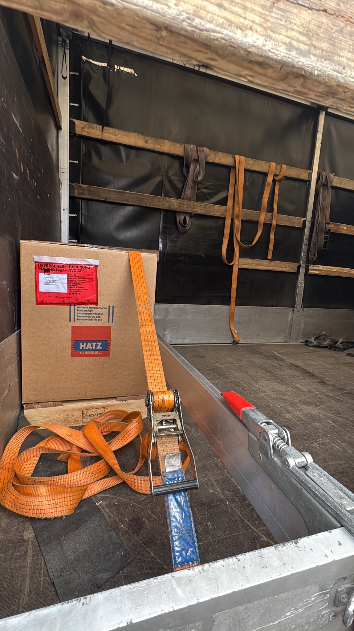 Karton zabezpieczony pasami w przestrzeni ładunkowej busa. Widoczne mocowania i elementy konstrukcyjne pojazdu. Bezpieczny transport towarów.