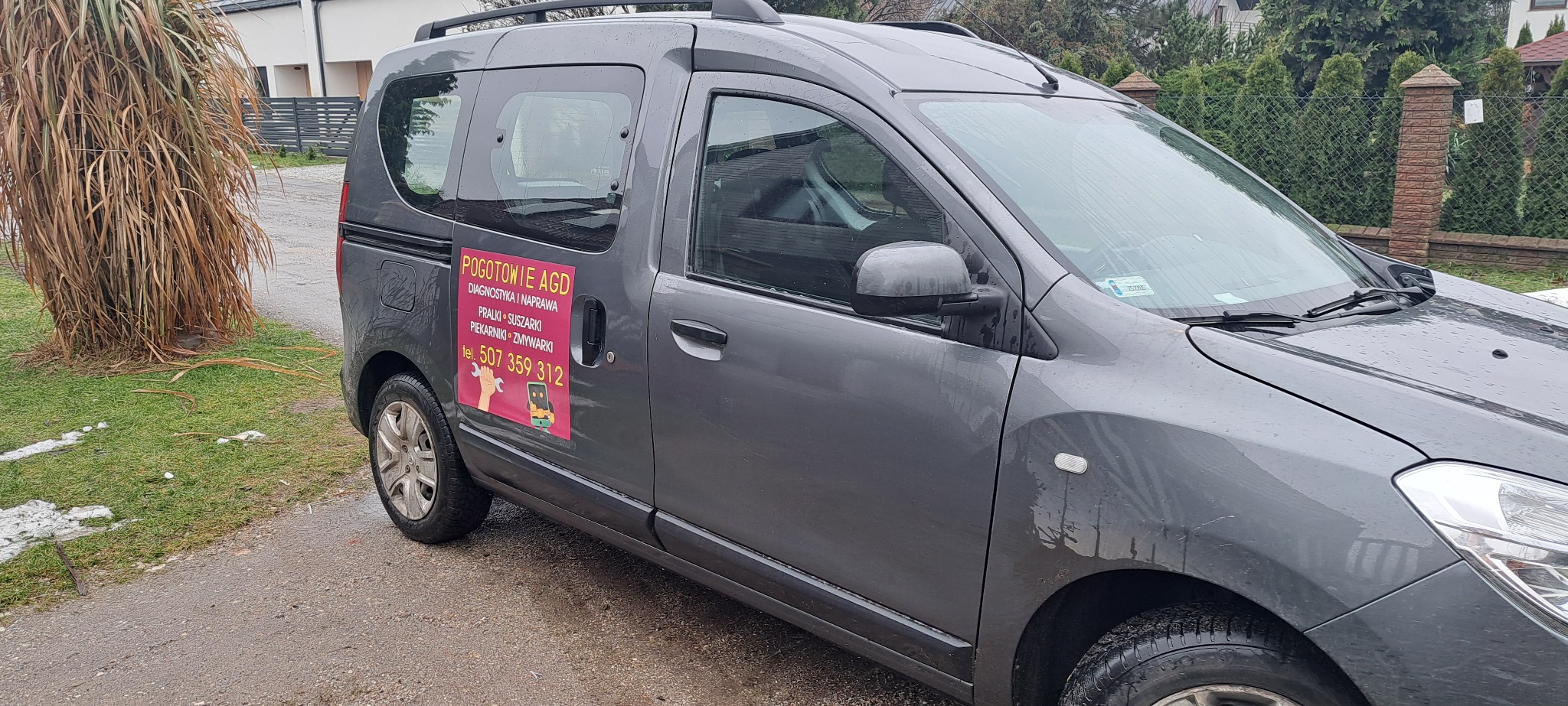 Szary samochód serwisowy z naklejką 'Pogotowie AGD' z numerem telefonu, zaparkowany na zewnątrz. Widoczne logo firmy na drzwiach.