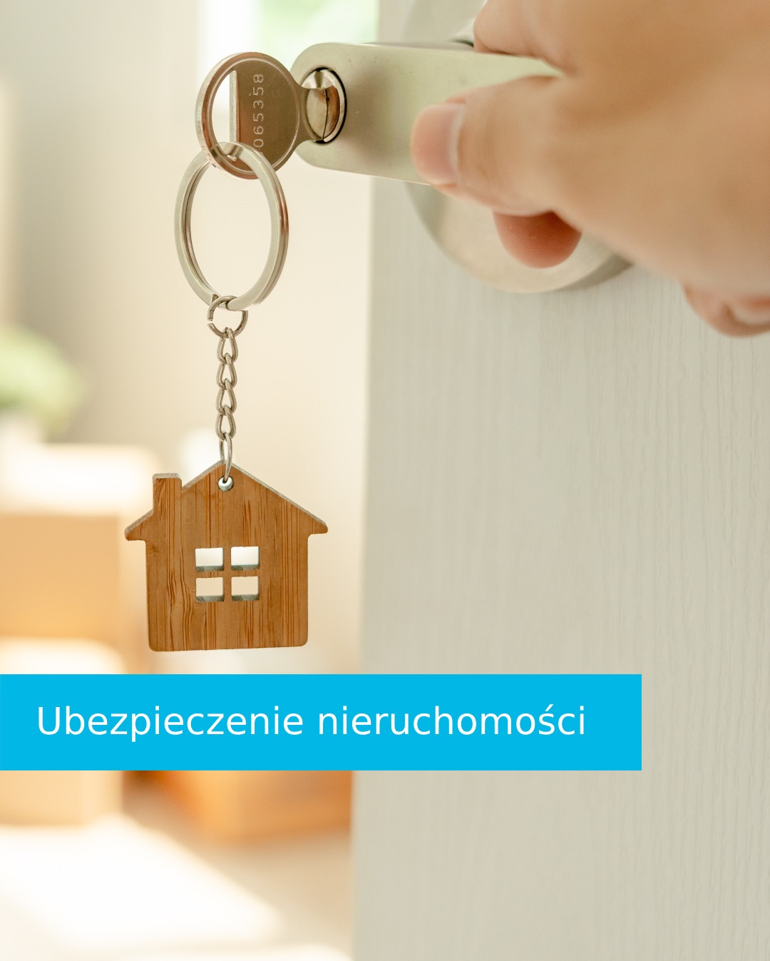 Klucz w zamku z brelokiem w kształcie domu. Symbolizuje bezpieczeństwo i ochronę nieruchomości. W tle jasne drzwi i kartony.