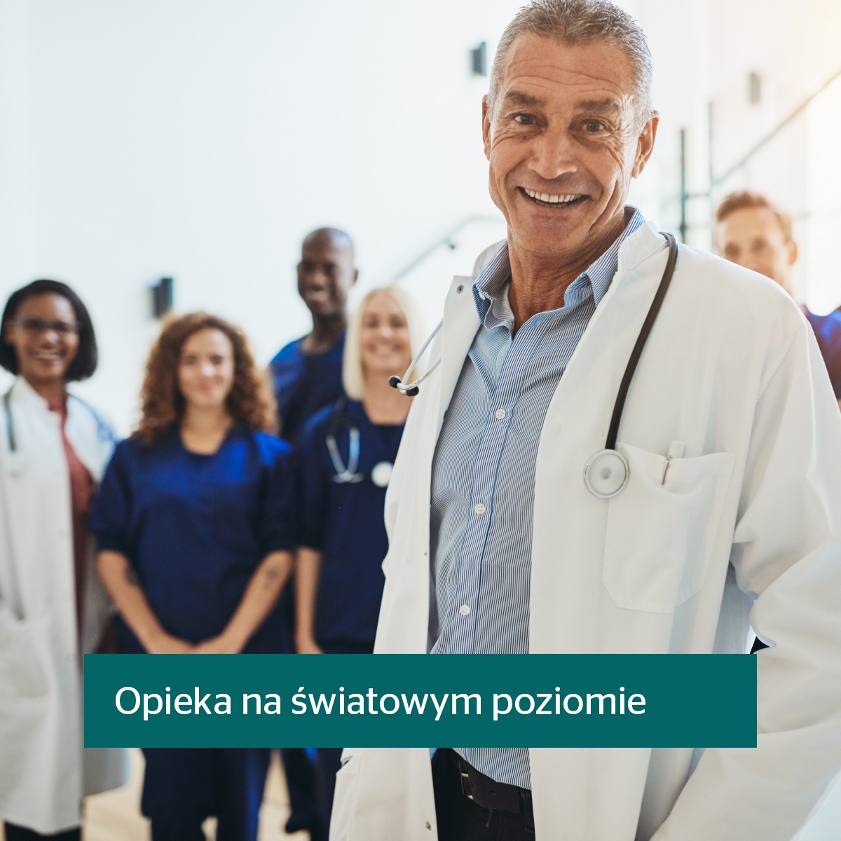 Uśmiechnięty lekarz w białym fartuchu ze stetoskopem na tle zespołu medycznego, reprezentujący profesjonalizm i opiekę zdrowotną.