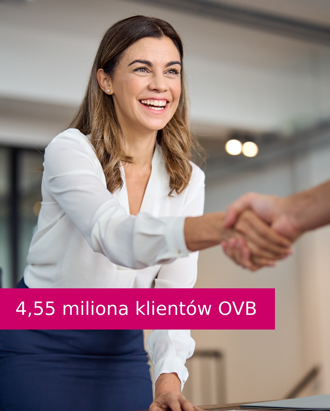Uśmiechnięta kobieta w białej bluzce wita się z klientem. W tle biuro. Różowy pasek z napisem: 4,55 miliona klientów OVB.